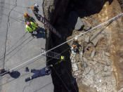 Rescuers descend into a sinkhole in Villa Nueva, Guatemala, Sunday, Sept. 25, 2022. Rescuers are searching for people who are believed to have fallen into the sinkhole while driving their vehicle, while four others were rescued alive from the scene on Saturday night. (AP Photo/Moises Castillo)