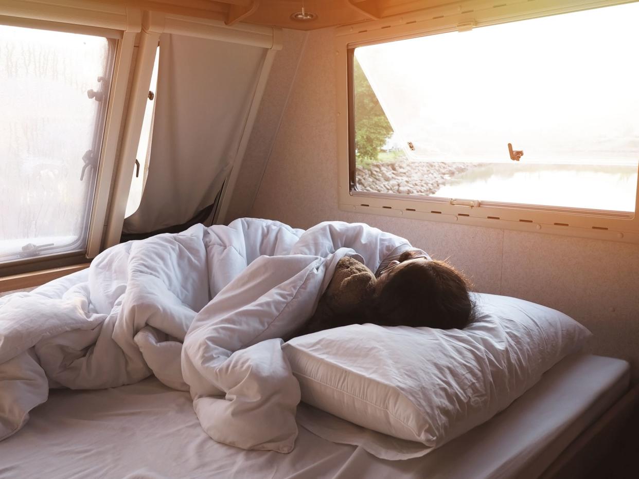 Back view of Asian girl sleeping on bed at camper van bedroom in the morning.