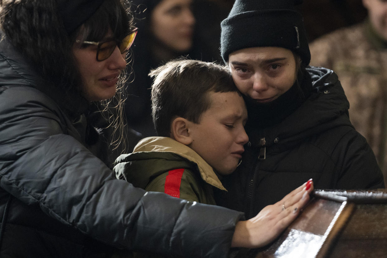 From left, mother Tetiana, brother Vlad and sister Olga, mourn above the coffin of 20 year-old soldier Vladyslav Belechynskyi, inside the Holy Apostles Peter and Paul Church in Lviv, western Ukraine, during a funeral, on Wednesday, Feb. 22, 2023. Belechynskyi died near Bakhmut, on Feb. 16. (AP Photo/Petros Giannakouris)