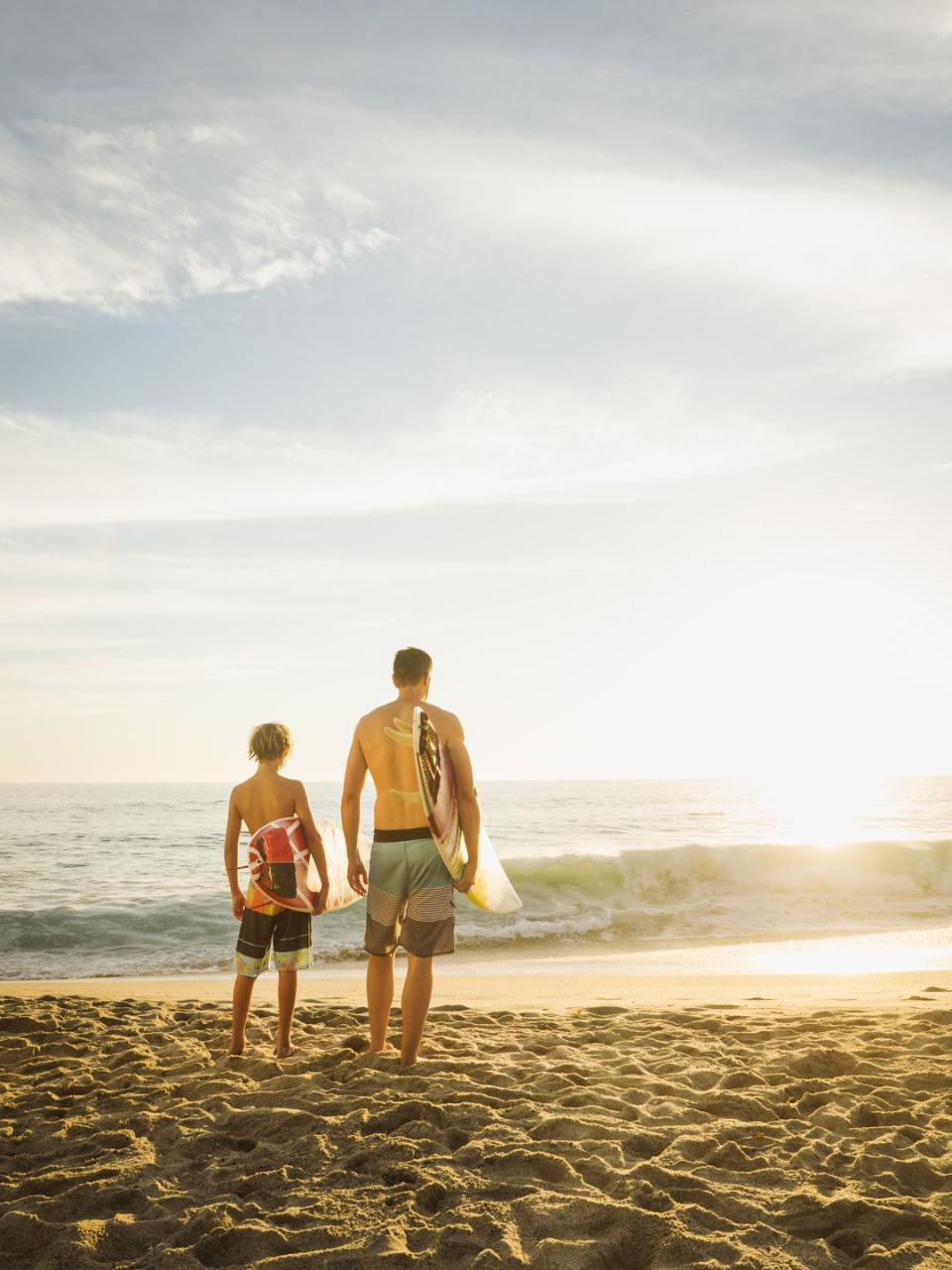 father and teen son with surfboards under arms looking at sea