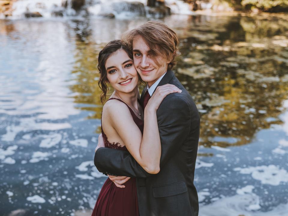 Prom dates hug each other in front of water.