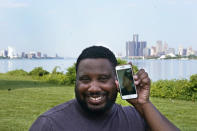 With the cities of Windsor, Ontario, Canada, left, and Detroit, right, seen in the background, Quintin Sweat Jr, poses with his fiancee Renee Harrison, seen on his phone, Tuesday, Aug. 3, 2021, on Belle Isle in Detroit. Sweat and Harrison live only 15 minutes apart by car, with the U.S.-Canada border between them. But the couple, who got engaged in 2019, has only been able to be together three times during the pandemic. (AP Photo/Carlos Osorio)