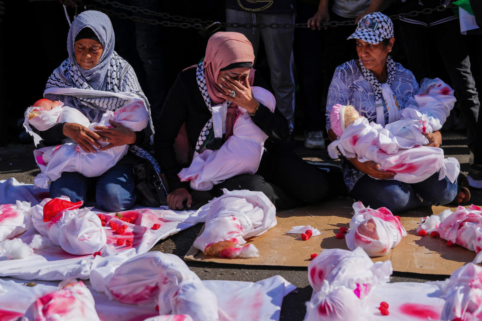 Women cradle mock bodies of dead Palestinian children wrapped in blood-stained blankets, during a sit-in following Friday prayer in solidarity with the Palestinian people in Gaza, in Beirut, Lebanon, Friday, Nov. 17, 2023. (AP Photo/Hassan Ammar)