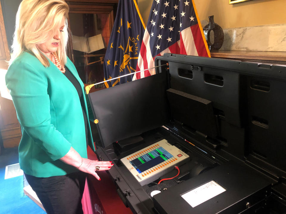 Indiana Secretary of State Holli Sullivan demonstrates an upgraded electronic voting machine at her Indiana Statehouse office in Indianapolis on March 17, 2022. State officials plan on spending about $12 million to add printers like the one at the right of the voting booth that display a printout allowing voters to see how their vote is recorded and create a paper record for the previously paperless machines. (AP Photo/Tom Davies)