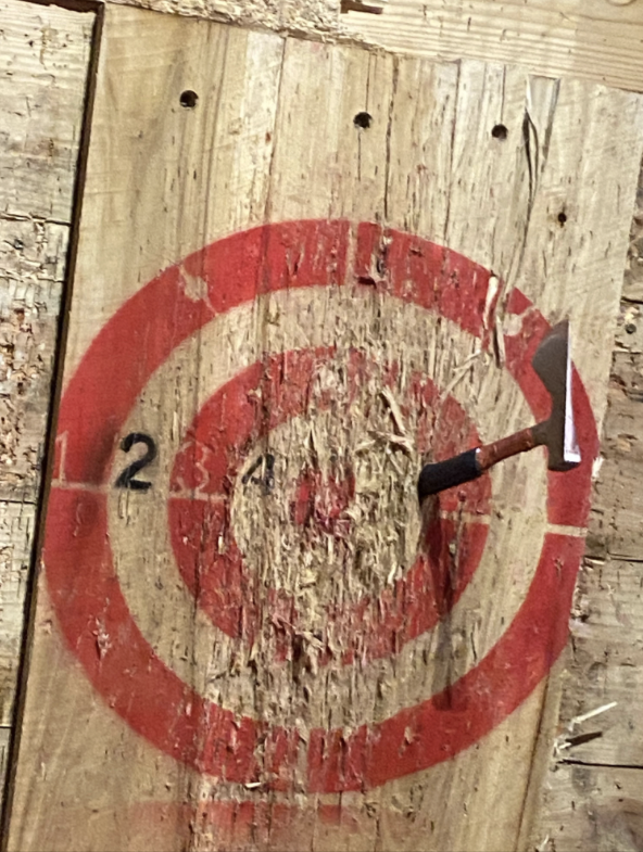 A wooden target with numbers 1 to 4 and a red bullseye, an axe is stuck in the bullseye