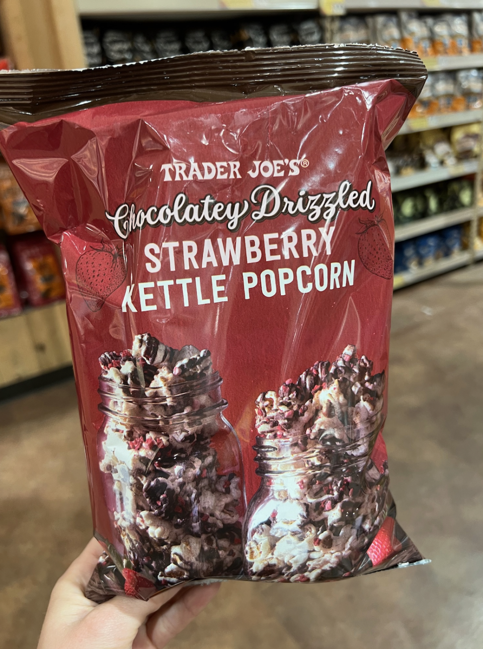 Hand holding a bag of Trader Joe's Chocolatey Drizzled Strawberry Kettle Popcorn