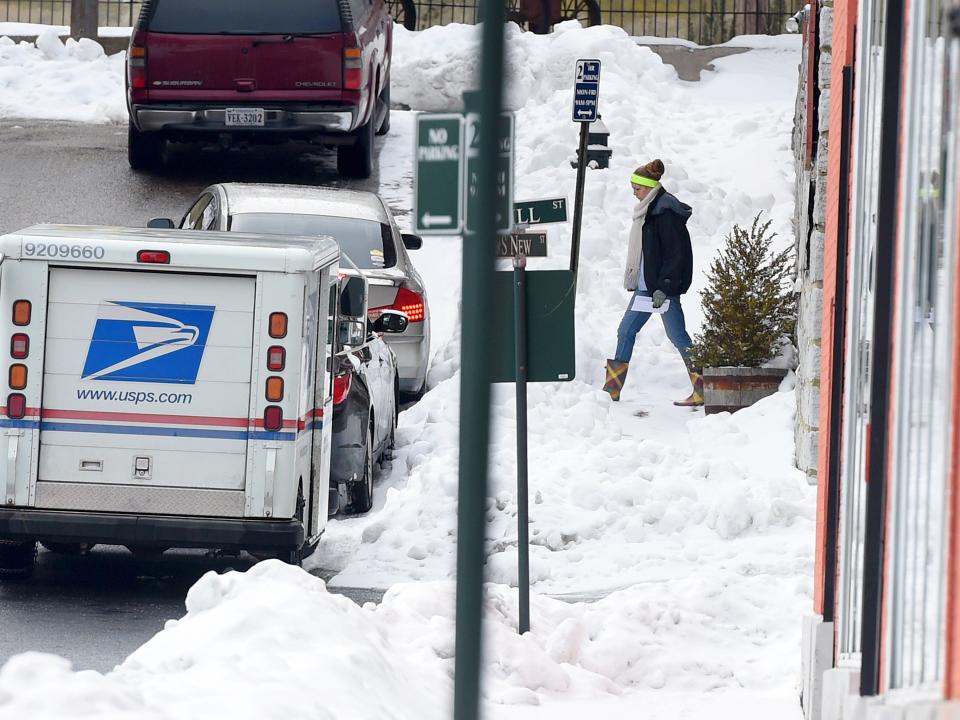 A United States Postal Service mail carrier has to walk through snow covering a sidewalk while making mail delivers along South New Street in downtown Staunton on Thursday, Feb. 26, 2015. 