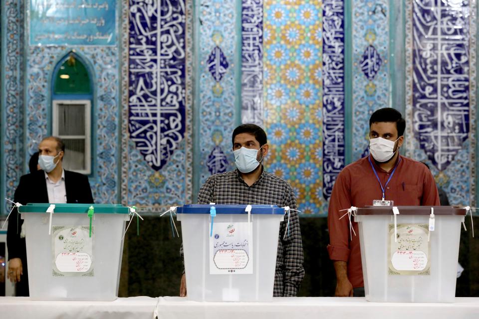 Iranian election officials wait for voters during the presidential election at a polling station in Tehran (AP)