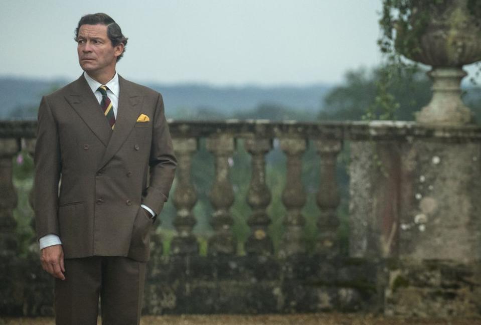 a man in a suit standing in front of a stone wall