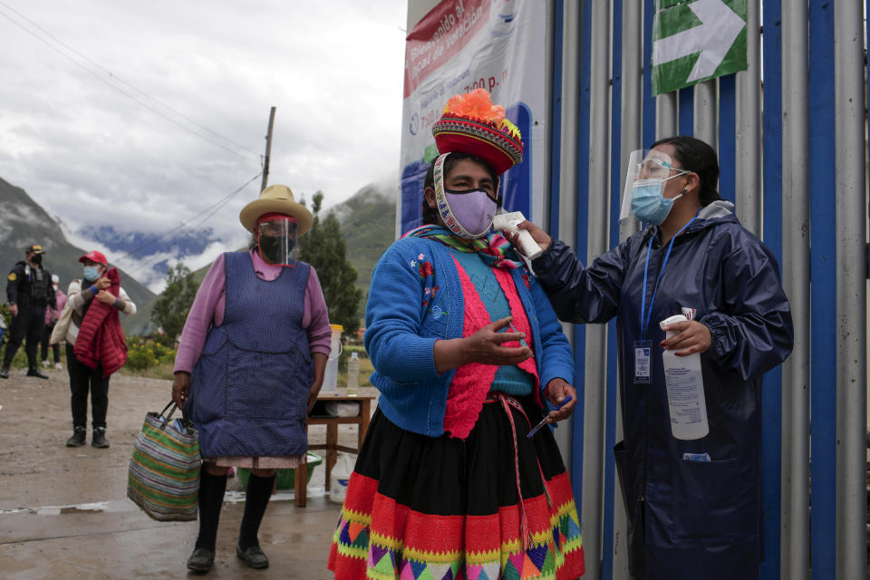 Voters wearing masks to curb the spread of the new coronavirus have their temperature measured at the entrance of a polling station during general elections in Ollantaytambo, Peru, Sunday, April 11, 2021. (AP Photo/Sharon Castellanos)