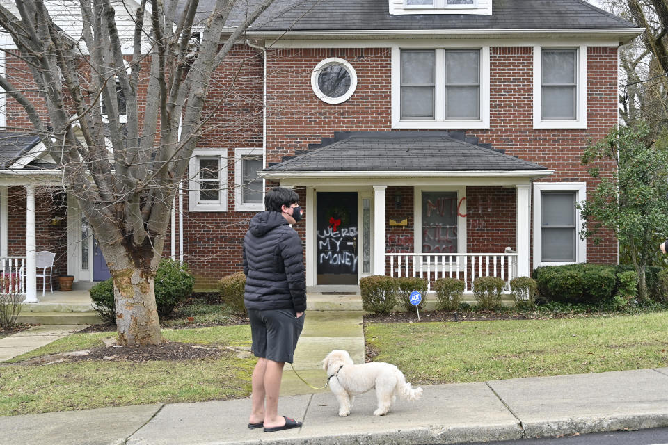 A neighbor looks at the spray paint on the front of the home of Senate Majority Leader Mitch McConnell, r, Ky., which was vandalized overnight in Louisville, Ky., Saturday, Jan. 2, 2021. (AP Photo/Timothy D. Easley)