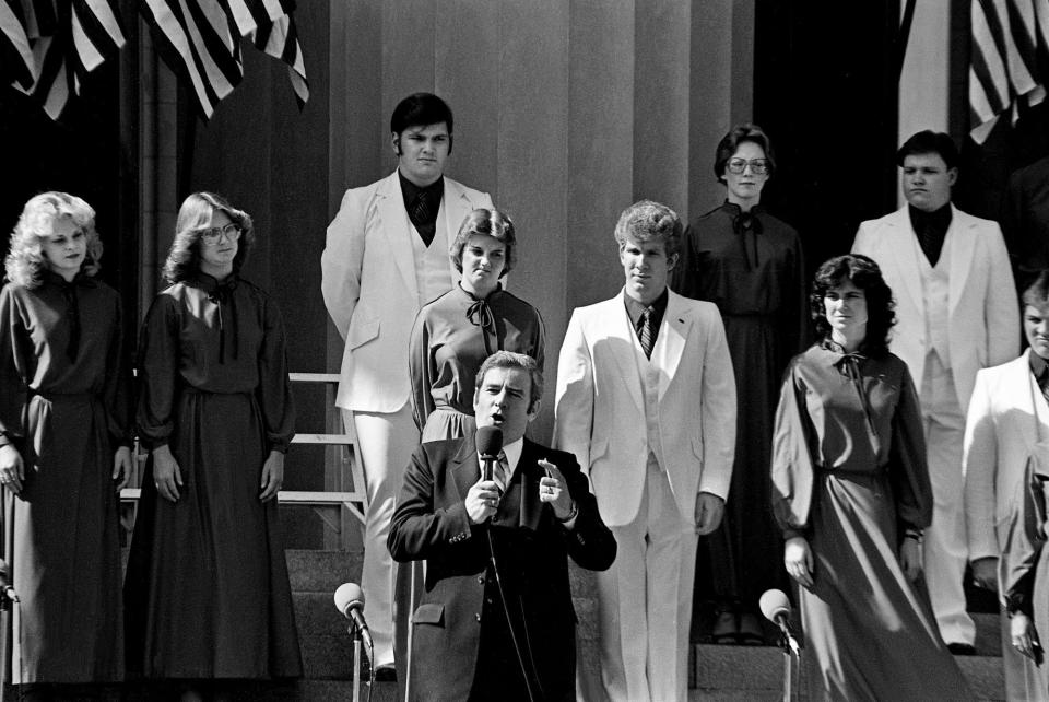 Backed by 32 choreographed singers in red, white and blue, the Rev. Jerry Falwell, pastor of the 17,000-member Thomas Road Baptist Church in Lynchburg, Va., presides over an "I Love America" rally at Legislative Plaza in Nashville on Oct. 15, 1979.