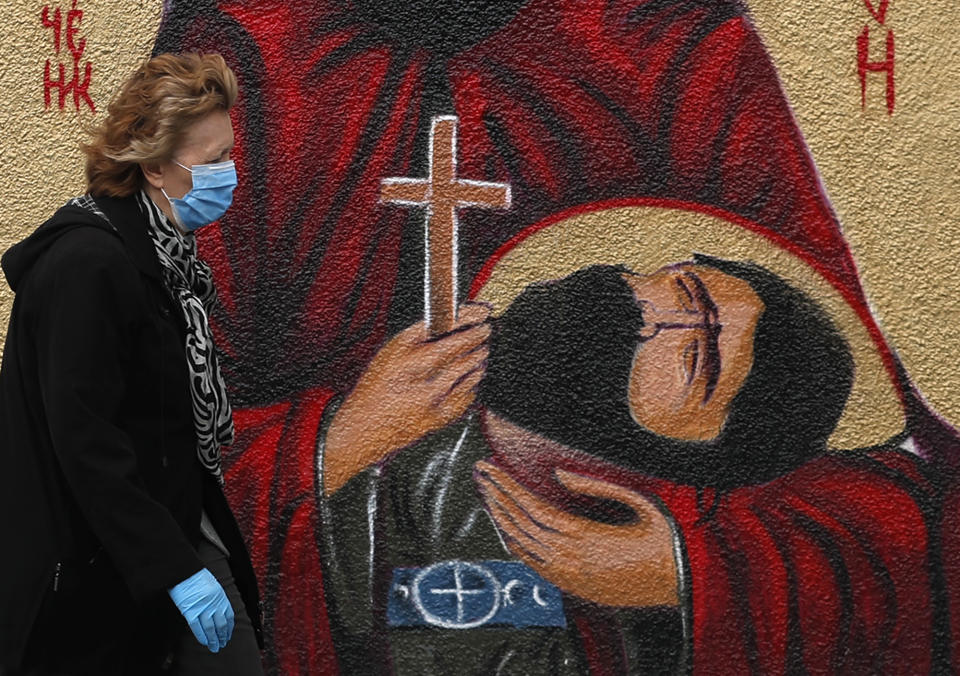 A woman wearing a protective face mask passes by graffiti depicting a Christian Orthodox icon in Belgrade, Serbia, Wednesday, May 27, 2020. (AP Photo/Darko Vojinovic)