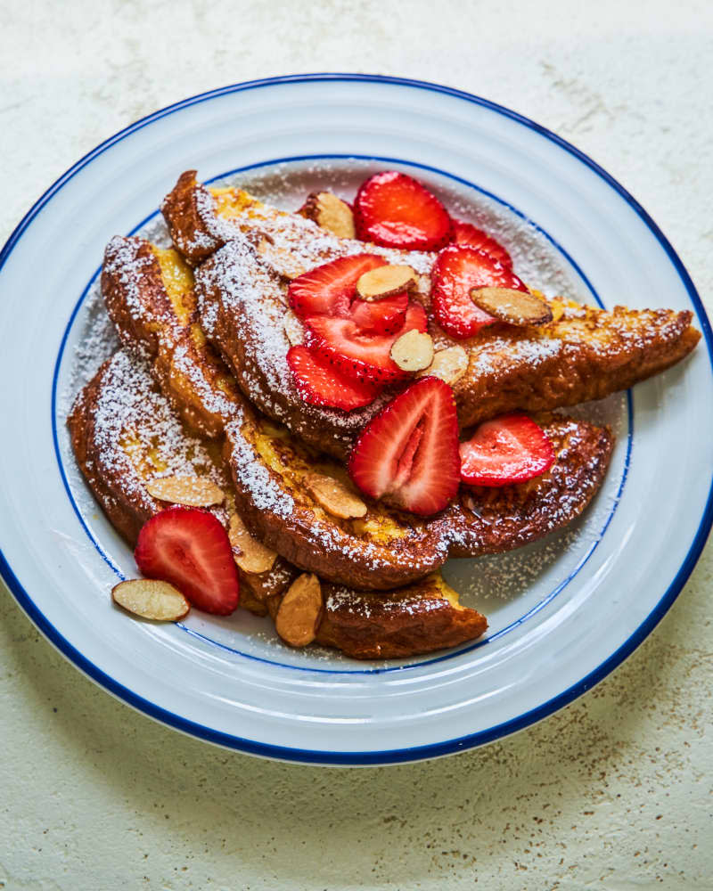 Pain Purdu, also known as French Toast, with sliced almond, sliced strawberries and powdered sugar on a white plate with a blue border