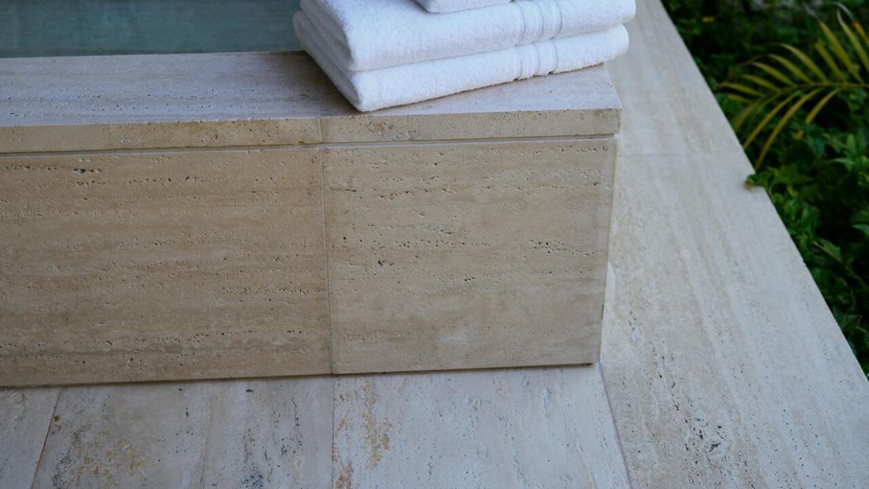 a stack of white towels on a wooden bench in front of a stone wall