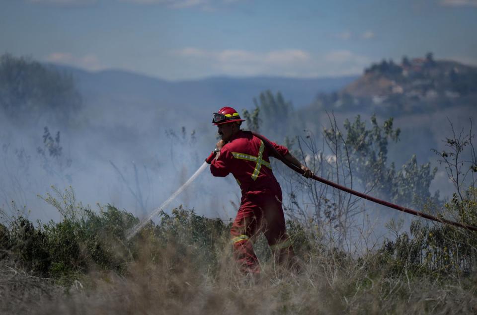 A firefighter directs water on a grass fire on an acreage behind a residential property in Kamloops, British Columbia (A)