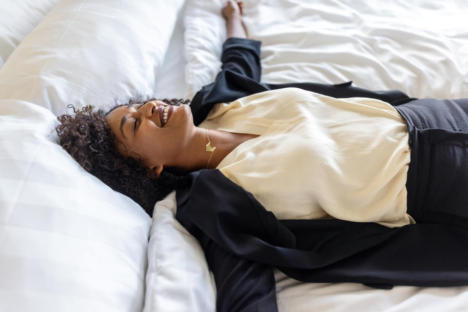 work Tired mid adult businesswoman lying on hotel bed after her trip. Tired woman in formal clothes resting on hotel bed with her arms outstretched and smiling.