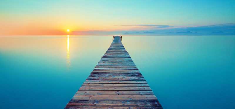 Serene image of a wooden dock going out into the ocean at sunset.