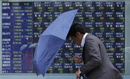 A man walks against strong wind and rain in front of a stock quotation board outside a brokerage in Tokyo October 2, 2013. REUTERS/Toru Hanai