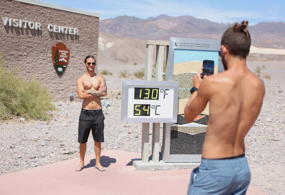 Gabriel Ambrus de Moraes, 29, (L) is photographed by his twin brother Pedro, both of Los Angeles, as he stands next to a digital display of an unofficial heat reading at Furnace Creek Visitor Center during a heat wave in Death Valley National Park in Death Valley, California, on July 16, 2023. Tens of millions of Americans braced for more sweltering temperatures Sunday as brutal conditions threatened to break records due to a relentless heat dome that has baked parts of the country all week. By the afternoon of July 15, 2023, California's famous Death Valley, one of the hottest places on Earth, had reached a sizzling 124F (51C), with Sunday's peak predicted to soar as high as 129F (54C). Even overnight lows there could exceed 100F (38C). (Photo by Ronda Churchill / AFP) (Photo by RONDA CHURCHILL/AFP via Getty Images)