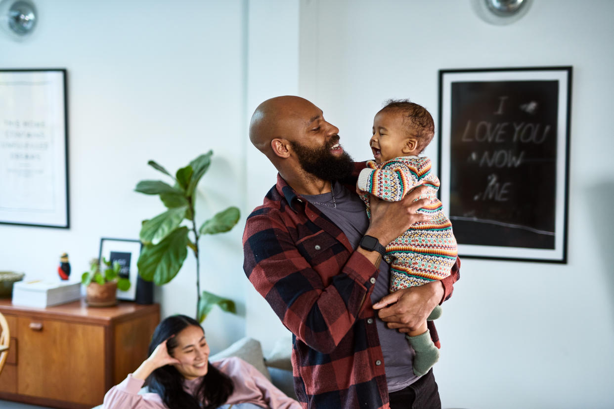 Father holding baby while mother sits in background 