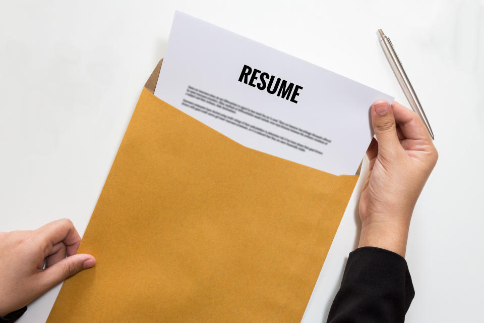 Hands remove a resume from a yellow folder. Image: Getty