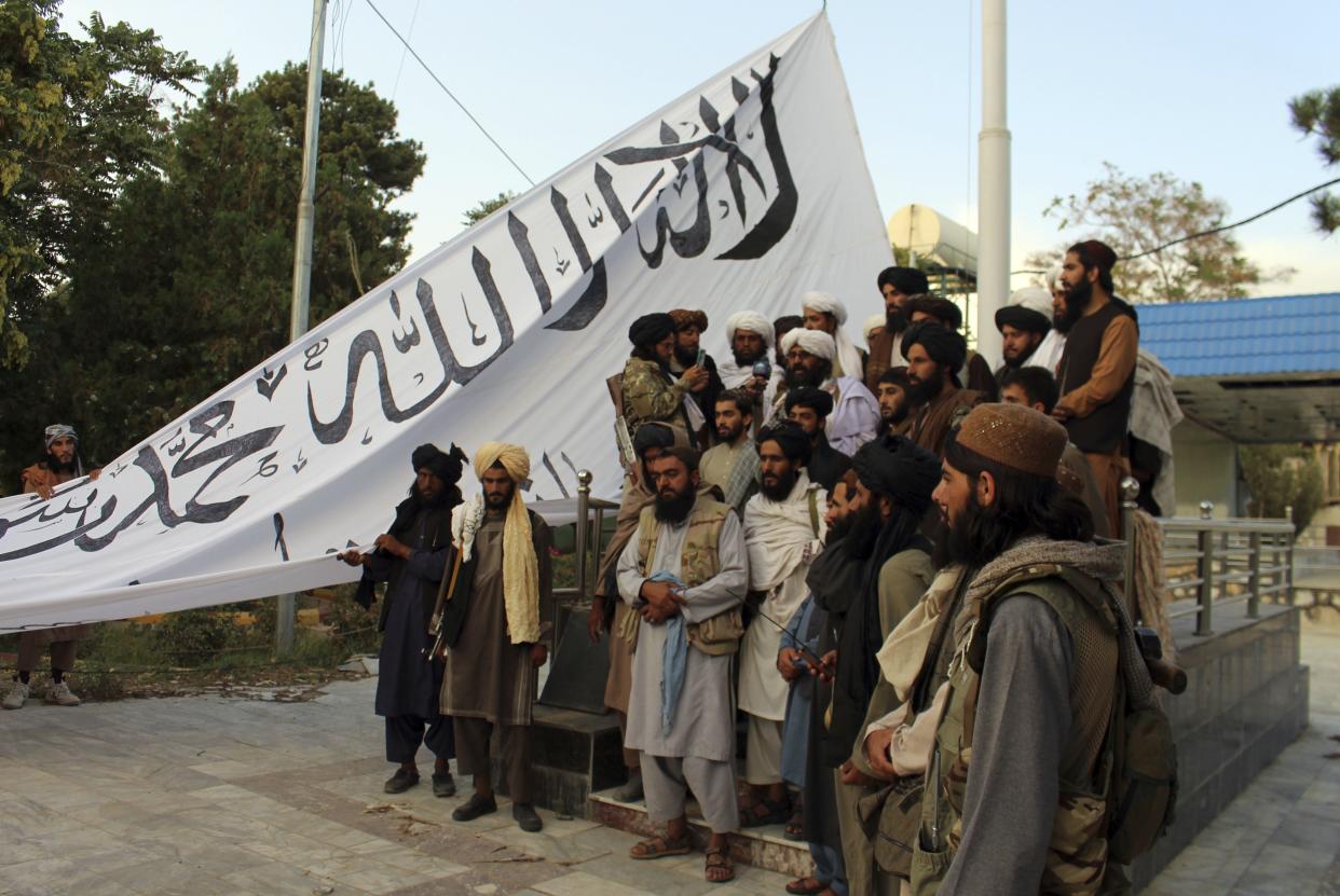 Taliban fighters pose for a photograph while Taliban fighters raise their flag at the Ghazni provincial governor's house, in Ghazni, southeastern, Afghanistan, Sunday, Aug. 15, 2021.