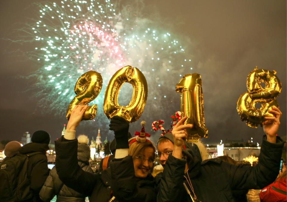 <p>People hold up balloons shaped as digits 2, 0, 1 and 8 as they watch fireworks over central Moscow during New Year celebrations. (Photo: Marina Lystseva/Getty Images) </p>