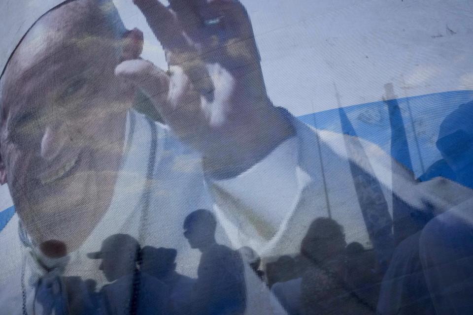 Numerosos fieles permanecen detrás de una pancarta con la imagen del papa Francisco cuando se disponen a caminar hacia la Catedral para asistir a una misa por los 15 años de la organización Familia Grande Hogar de Cristo dedicada a rehabilitar a drogadictos y festejar el 10 aniversario de Francisco como Papa, en Luján, Argentina, el sábado 11 de marzo de 2023. Francisco salió de Argentina en febrero de 2013 para asistir al cónclave en la que fue elegido sucesor de Benedicto XVI el 13 de marzo. (AP Foto/Natacha Pisarenko, Archivo)Francis left Argentina in February 2013 to attend the conclave that elected him as the successor to Benedict XVI on March 13. (AP Photo/Natacha Pisarenko)