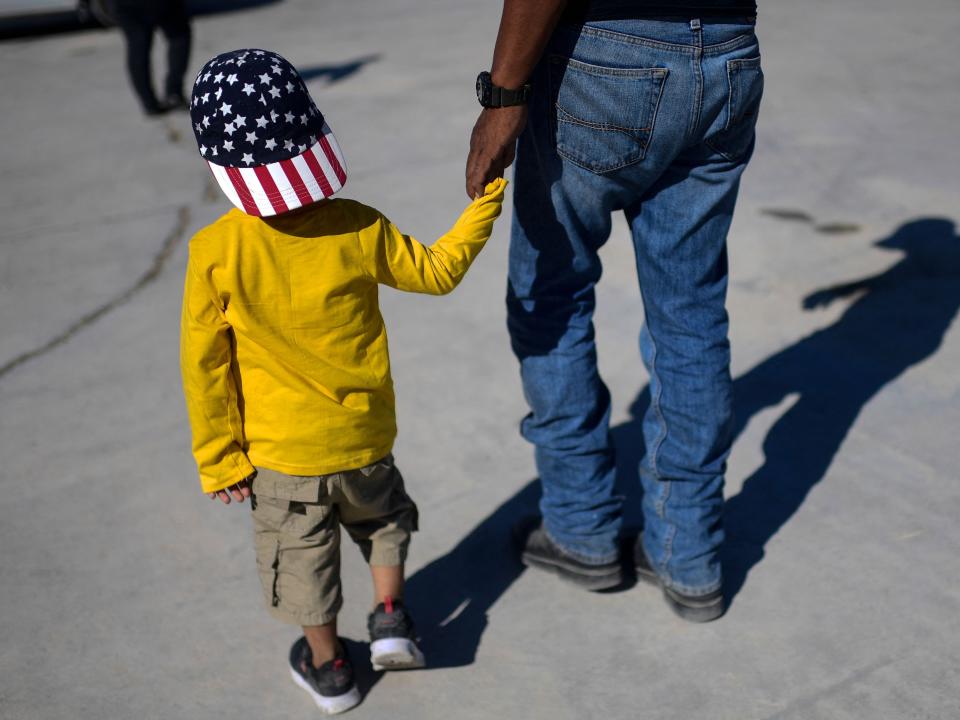 Haitian migrant holding hand of child wearing an American flag, stars-and-stripes, hat.