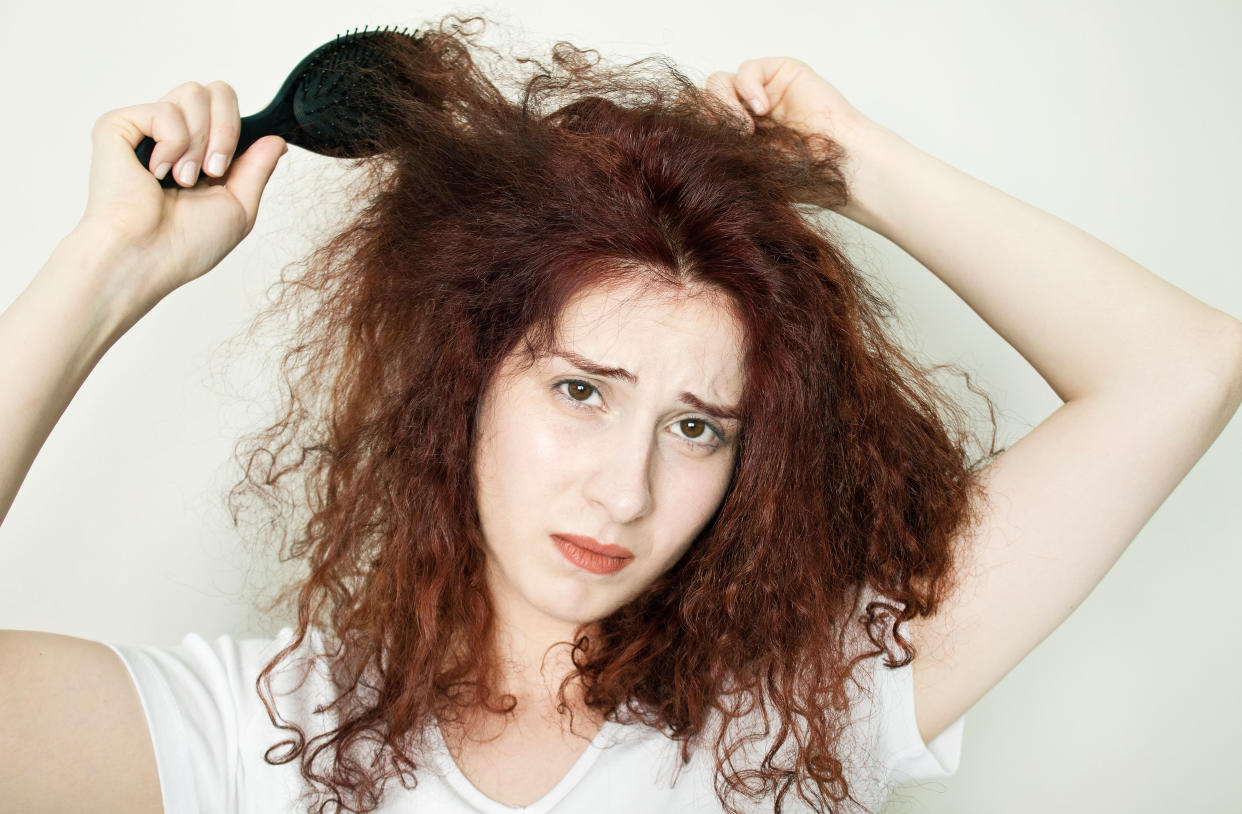 A woman with curly hair trying to comb her tangled locks.