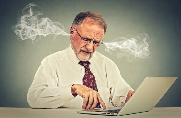 A man using a laptop computer with smoke coming out of his ears.