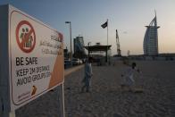 File - In this Friday, March 20, 2020 file photo, two laborers play tag near a sign warning people to maintain a distance from each other over the outbreak of the new coronavirus in front of the sail-shaped Burj Al Arab luxury hotel in Dubai, United Arab Emirates. The United Arab Emirates has closed its borders to foreigners, including those with residency visas, over the coronavirus outbreak, but has yet to shut down public beaches and other locations over the virus. (AP Photo/Jon Gambrell, File)