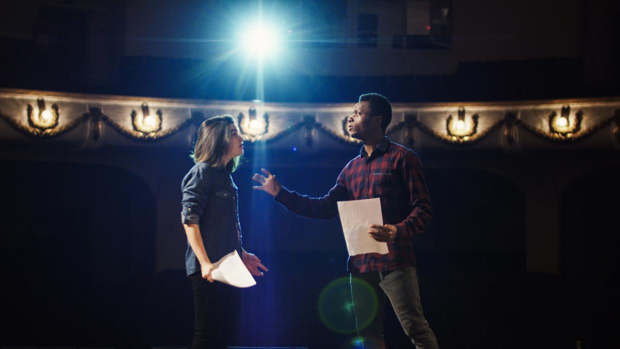 Medium shot of an actor and actress rehearsing a scene in the theater while holding their scripts.