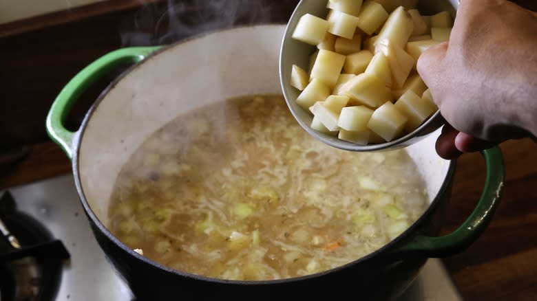 adding potatoes to pot of soup