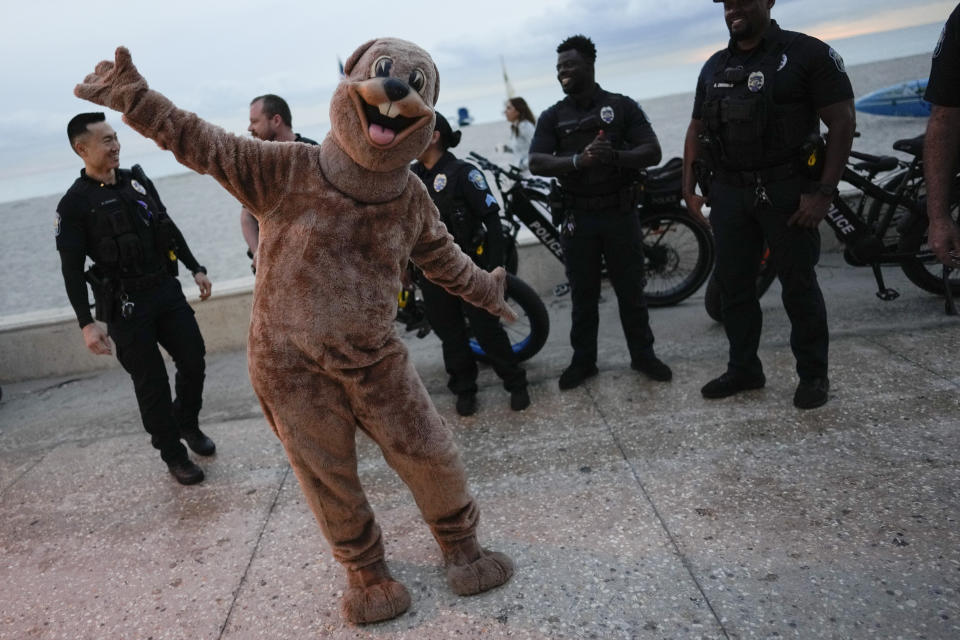 A local version of Punxsutawney Phil jokes around in front of police as people gather on the beach boardwalk at dawn to celebrate Groundhog Day, in Hollywood, Fla., Friday, Feb. 2, 2024. Hollywood's version of Phil saw his shadow and predicted "six more weeks of tourism" for the area, before dozens of celebrants sang the national anthem then ran into the ocean as part of a local Groundhog Day tradition that dates back twenty years. (AP Photo/Rebecca Blackwell)