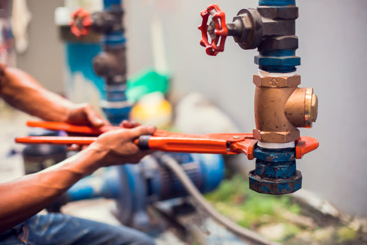 Plumber using a wrench to repair and remove the water supply pipe and valve. Plumbers working using orange pipe wrenches with blurry motor pump motor.