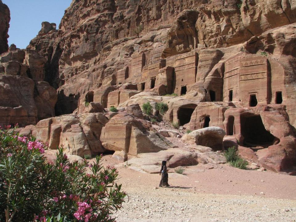 This April 23, 2016 photo shows a woman walking past burial buildings carved out of red canyons in Petra, an ancient city filled with architectural and artistic gems in Jordan. This Middle Eastern country delivers a blockbuster list of iconic ancient monuments, otherworldly landscapes and warmhearted hospitality, with Petra as its tourism jewel. (Giovanna Dell'Orto via AP)