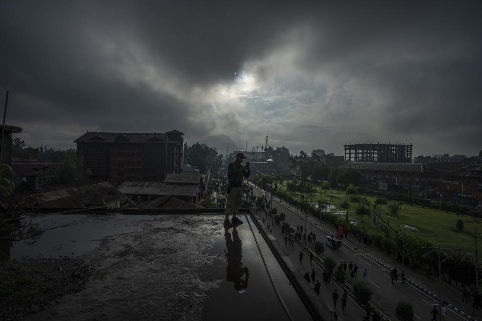 A policeman guarding atop a building films Kashmiri Shiite Muslims participating in a Muharram procession in Srinagar, Indian controlled Kashmir, Thursday, July 27, 2023. Muharram is a month of mourning for Shiite Muslims in remembrance of the martyrdom of Imam Hussein, the grandson of the Prophet Muhammad. (AP Photo/Dar Yasin)