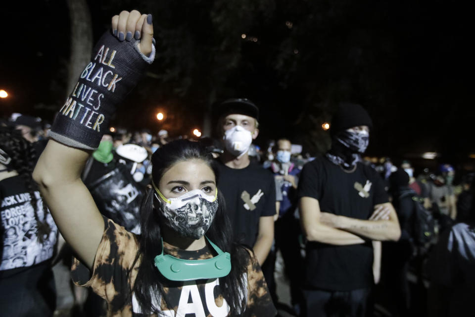 A demonstrator raises her fist while listening to a speech during a Black Lives Matter protest at the Mark O. Hatfield United States Courthouse Thursday, July 30, 2020, in Portland, Ore. After days of clashes with federal police, the crowd outside of the federal courthouse remained peaceful Thursday night. (AP Photo/Marcio Jose Sanchez)