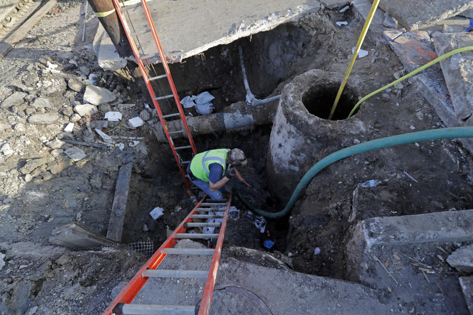 FILE - In this Jan. 31, 2018, file photo, workers fix a sewer main below the sidewalk in Mid City New Orleans. The Southern tourist destination is grappling with longstanding infrastructure challenges, including potholes, drainage problems and sporadic drinking water issues. (AP Photo/Gerald Herbert, File)