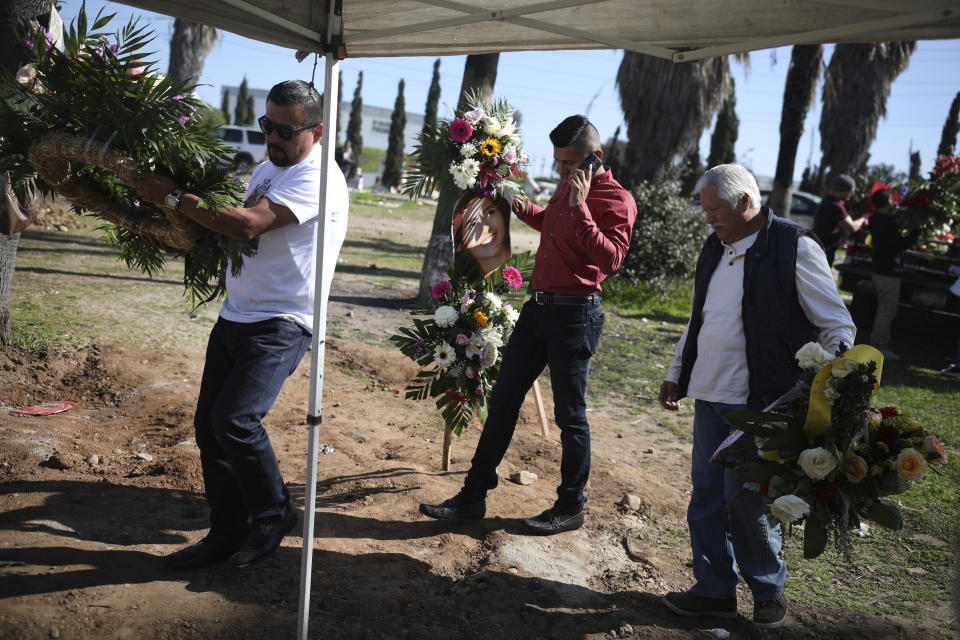 Juan, left, who has been arrested in connection with the disappearance and murder of Marbella Valdez, carries a floral arrangement to her grave, followed by her ex-boyfriend Jairo Solano, during her burial at a cemetery in Tijuana, Mexico, Friday, Feb. 14, 2020. Juan, who sent her gifts and brought food for her friends, demanded police solve her case after the 20-year-old law student's body, beaten, bound and strangled was found at a Tijuana garbage dump. Juan has insisted on his innocence. (AP Photo/Emilio Espejel)