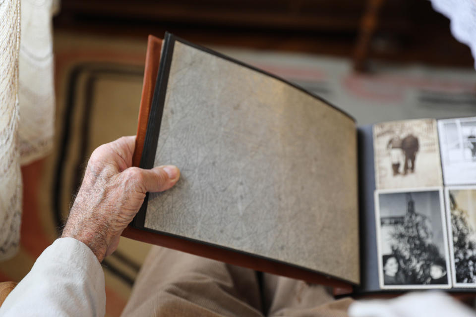 A person looks at a photo album, holding a page with no images on the left while viewing multiple black and white photos on the right