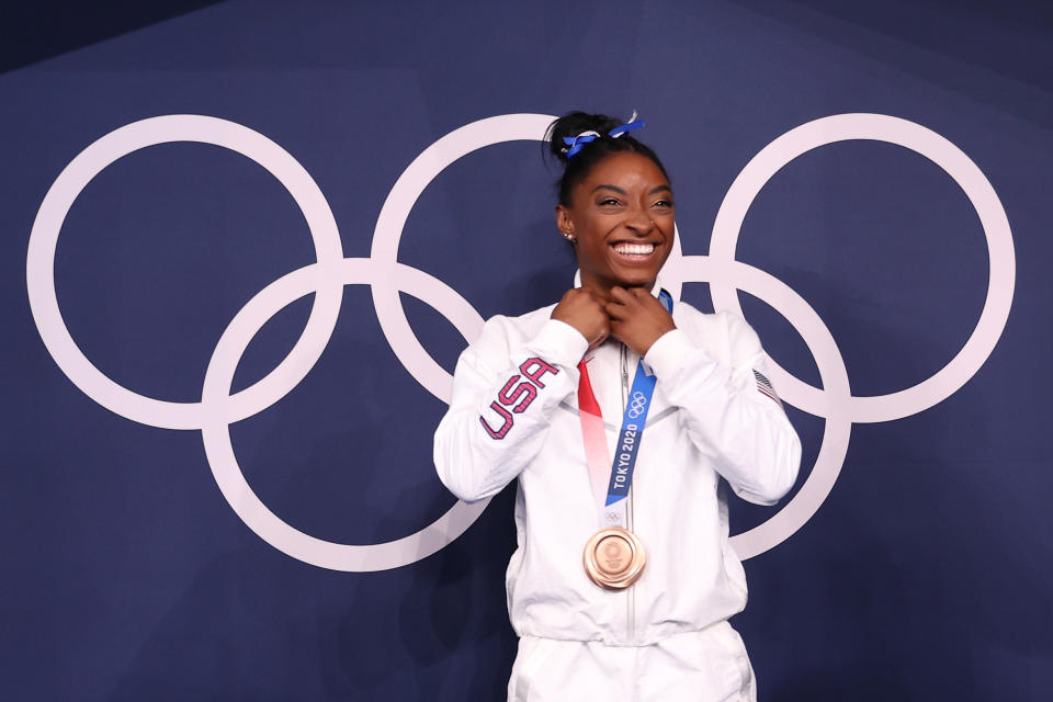 Biles poses in front of the Olympic rings with her bronze medal around her neck
