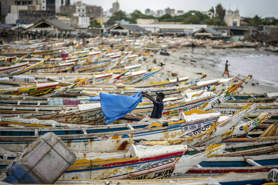 A fisherman dries a sheet next to fishing boats that are grounded because demand for fish dries up during the upcoming Islamic holiday of Eid al-Adha when people slaughter sheep to eat and when the fishermen return home to their families, on the beach in Dakar, Senegal Thursday, July 30, 2020. Even in the best of times, many Muslims in West Africa scramble to afford a sheep to slaughter on the Eid al-Adha holiday, a display of faith that often costs as much as a month's income, and now the coronavirus is wreaking havoc on people's budgets putting an important religious tradition beyond financial reach. (AP Photo/Sylvain Cherkaoui)