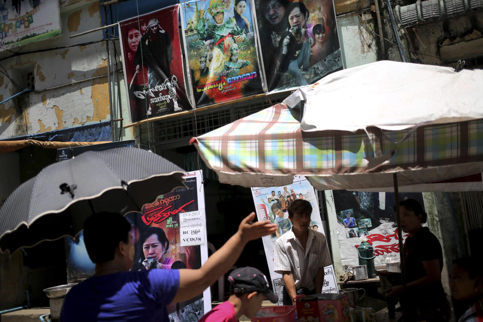 In this Tuesday, Aug. 13, 2013 photo, store vendors stand near movie posters amidst the tightly packed enclave of video production houses, movie-poster design studios and worse-for-wear apartment buildings that serves as the tattered ground zero of the Burmese movie industry, in downtown Yangon, Myanmar. In the heart of Yangon's Little Hollywood, actors have been struggling for work as Myanmar opens up to a world brimming with pop-culture choices, and those who specialize in villainy have been hit particularly hard. They sit on tiny plastic chairs, glowering and stalking an ever-more-elusive quarry: a day's work. (AP Photo/Wong Maye-E)