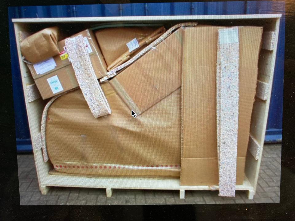 A photo of a seemingly dismantled piano wrapped in paper inside a moving crate.