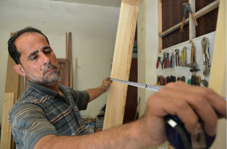 Syrian furniture maker Hussam Obayd measures wood at his workshop in the town of Saqba