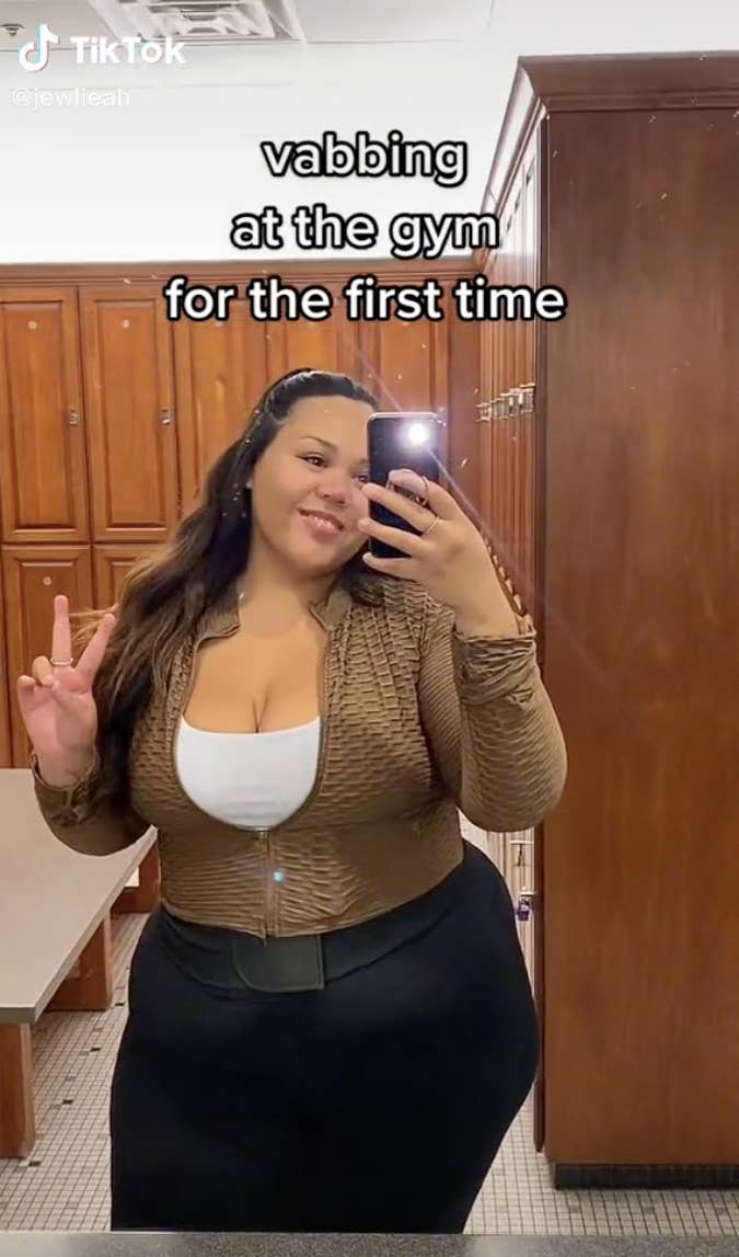 TikTok screenshot of woman taking a selfie in a bathroom with the caption "vabbing at the gym for the first time"