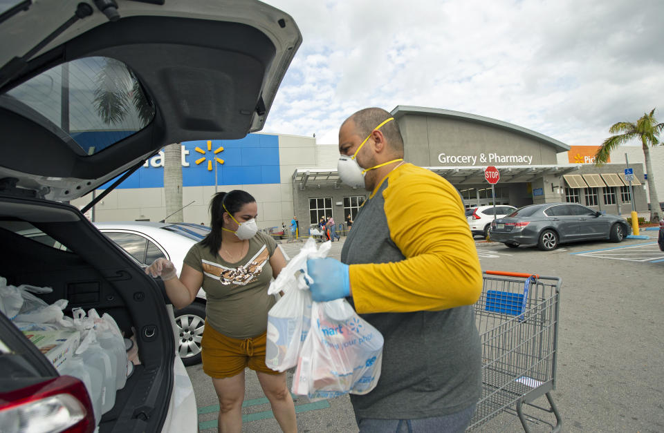 FILE - In this Sunday, April 5, 2020, file photo, Joel Porro and Lizz Hernandez wear gloves and protective masks as they put bags in the trunk of their car after shopping at a Walmart Supercenter amid the coronavirus pandemic, in Miami. (David Santiago/Miami Herald via AP, File)